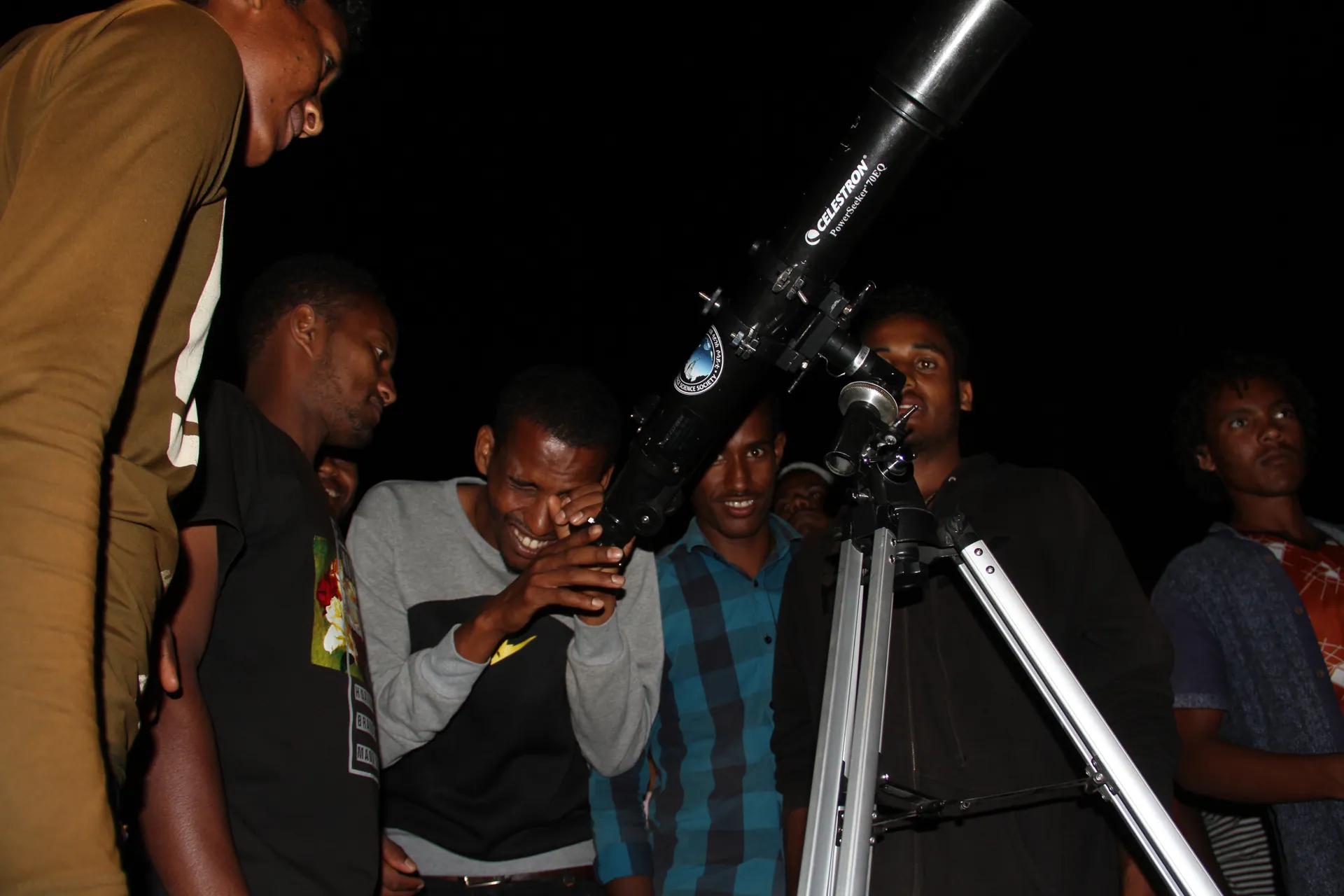 Young people look through a telescope at night in Adama