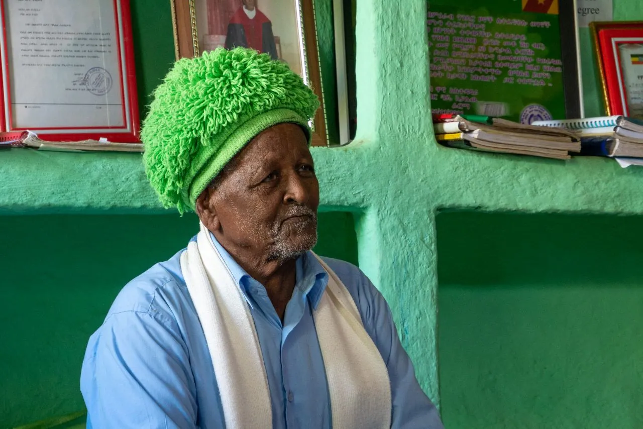An elder in a green hat, in a classroom
