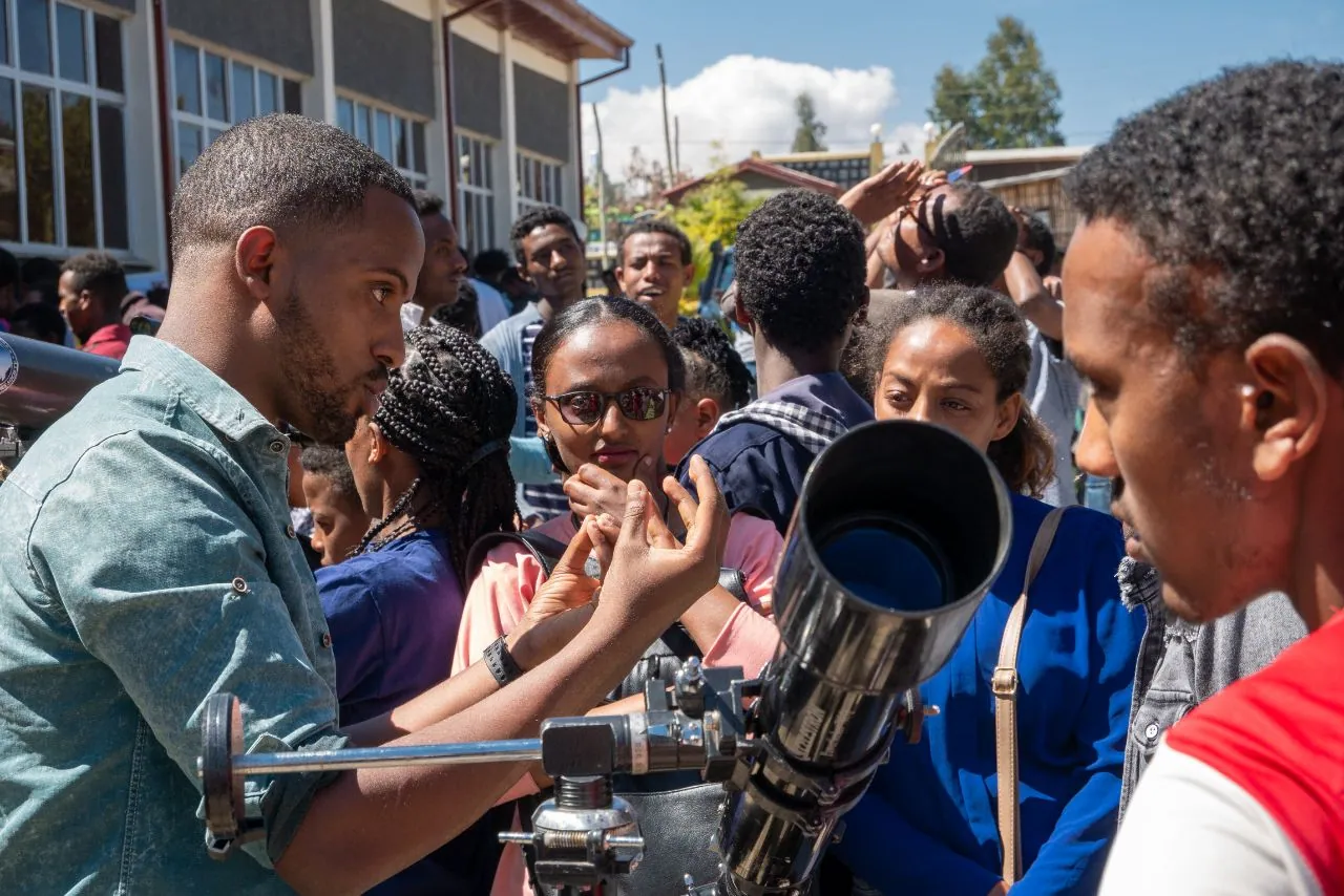 Students line up at a telescope outside a school