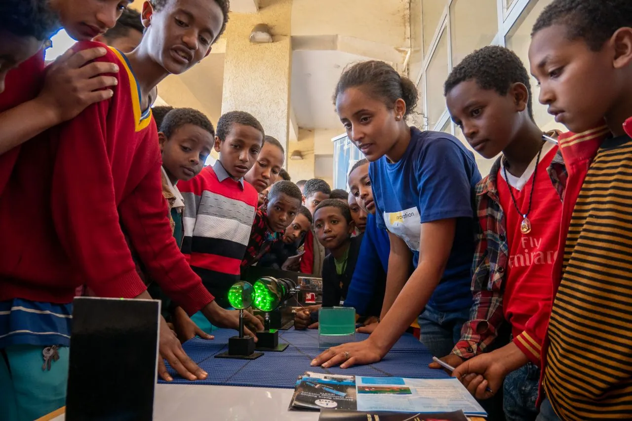 Children lean over a table of optics with a team member