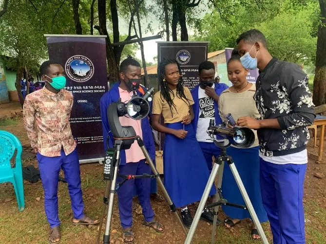 Students in masks show telescopes in front of the Society's banners