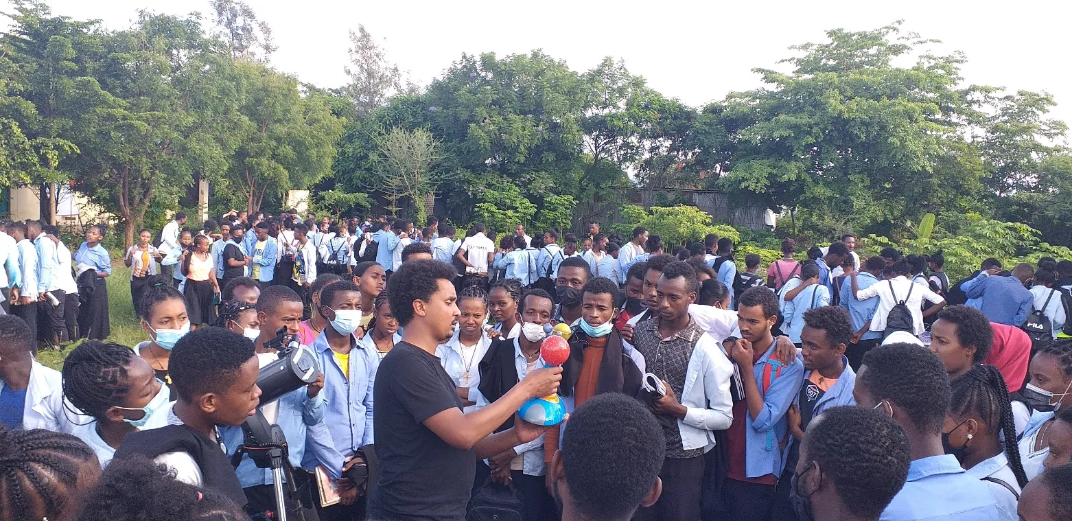 A team member speaks to a crowd of students in blue uniforms