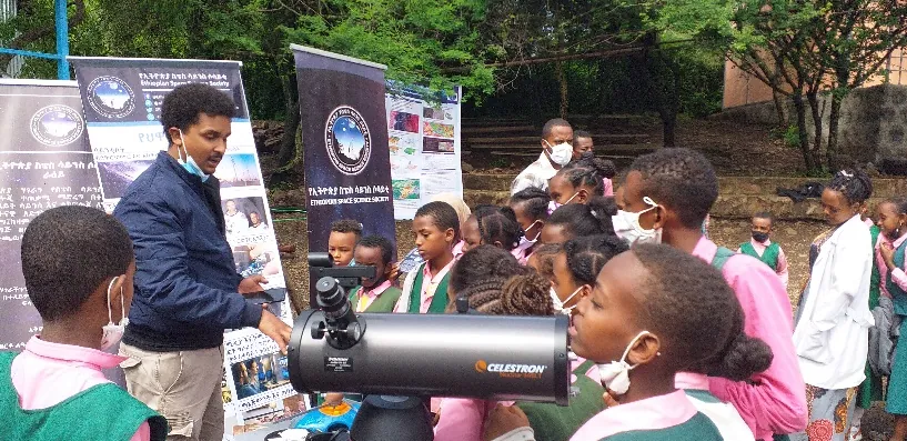 Schoolchildren in masks gather round a telescope
