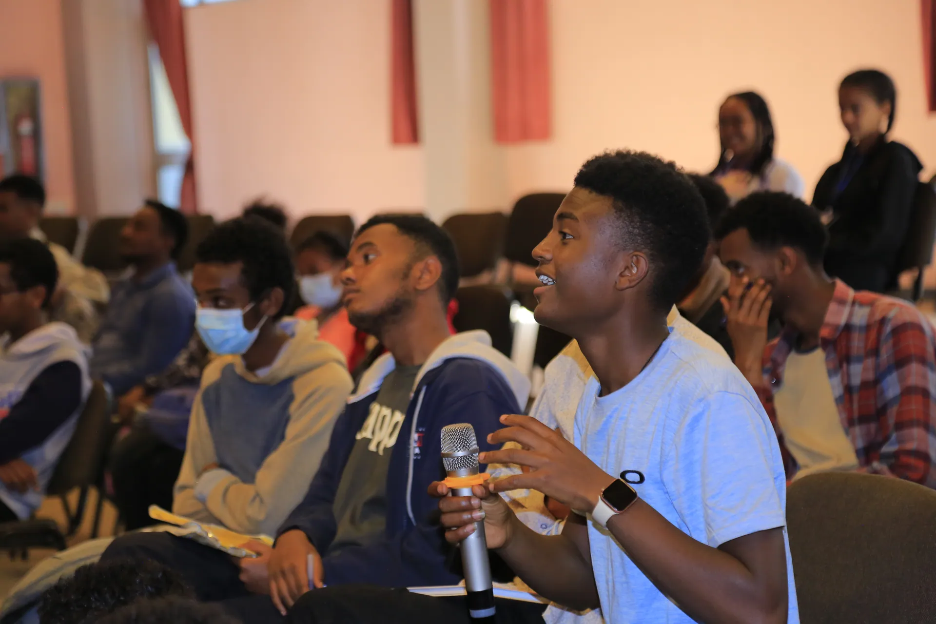 A young man in the audience smiles as he asks a question