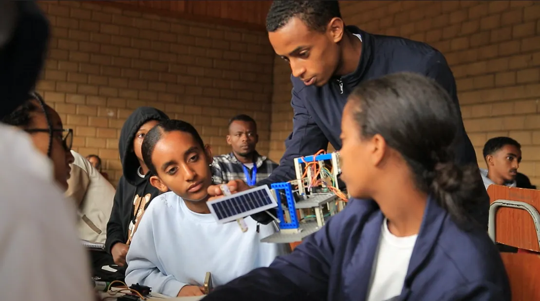 A trainer holds up a model satellite for his trainees