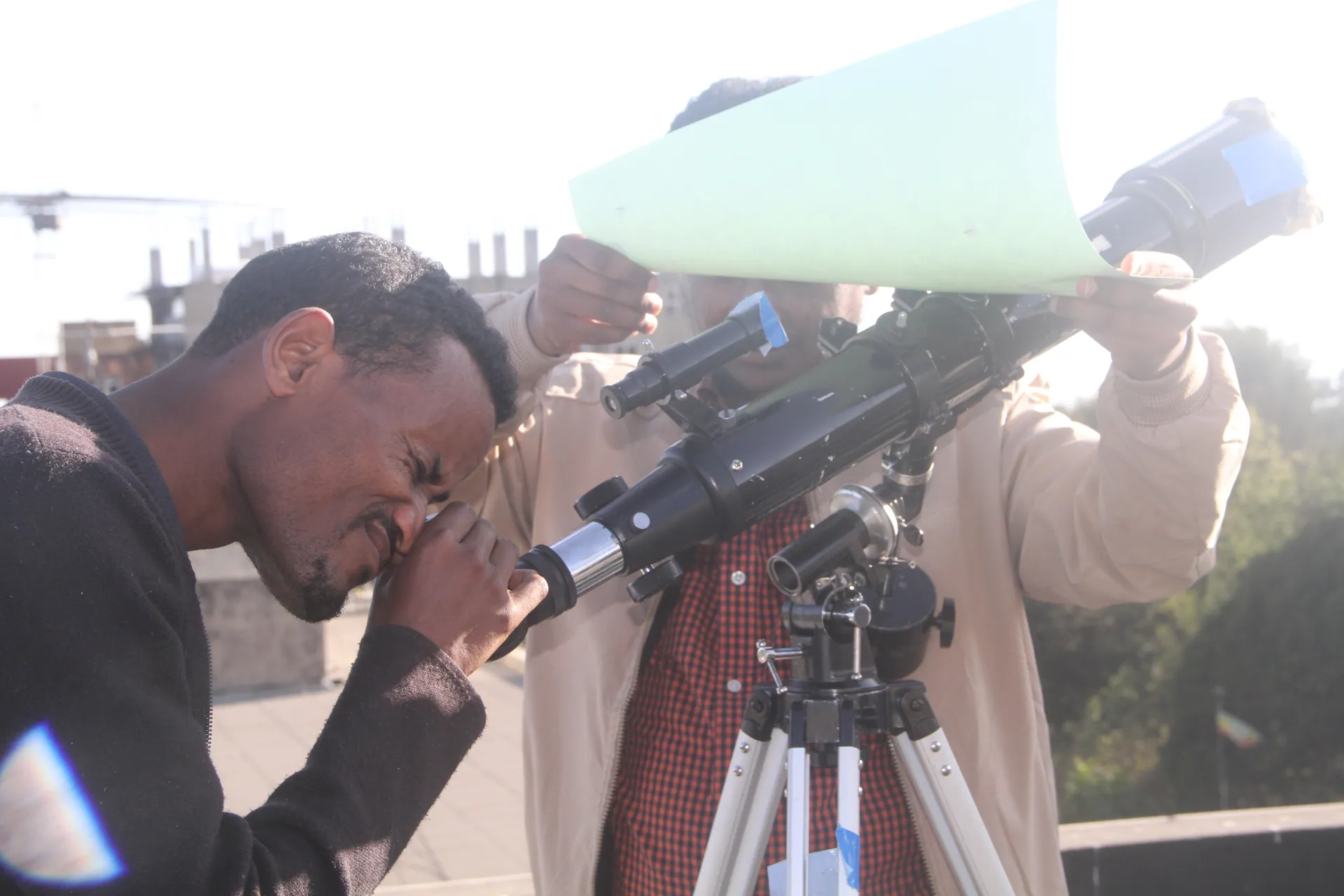 A teacher looks through a telescope while another catches the Sun on paper